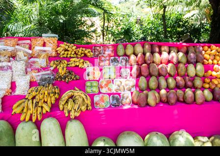 Un colorato banco di frutta all'aperto espone mango, banane, anguria e spuntini confezionati. Foto Stock