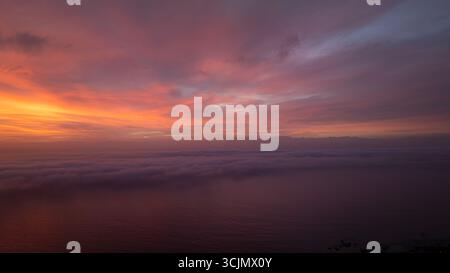 Vista aerea di un tramonto spettacolare che si illumina di arance ardenti e di soffici viola sull'oceano, che delineano la terra sottostante, città del Capo, Capo Occidentale, Sud Africa. Foto Stock