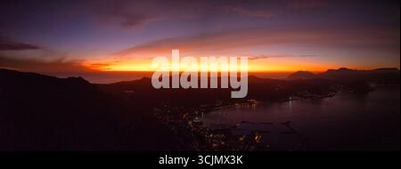 La vista aerea di un tramonto ardente dipinge il cielo sopra la sagoma di Table Mountain e le luci della città, città del Capo, Capo Occidentale, Sud Africa. Foto Stock