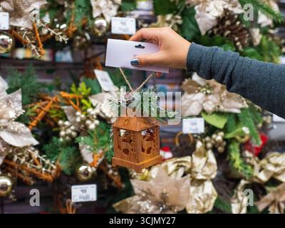 Una mano regge una piccola lanterna di Natale in legno ornata da verde e coni di pino. Foto Stock