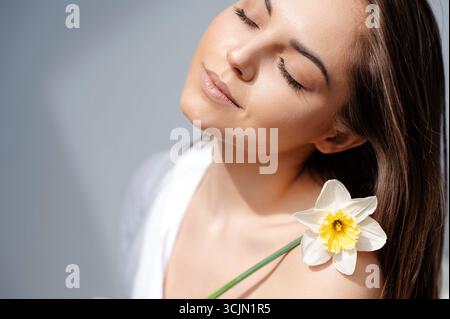 Tenera signora che tiene fiori di narcisi in posa su sfondo grigio studio Foto Stock