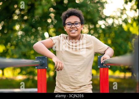 Adolescente dai capelli ricci che si allena al parco giochi e sembra eccitata Foto Stock