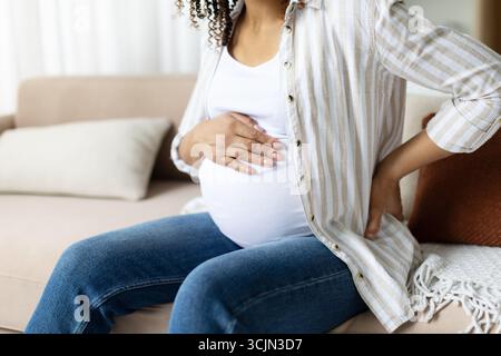 Primo piano di una donna incinta che tiene le mani sulla pancia e tocca la schiena Foto Stock
