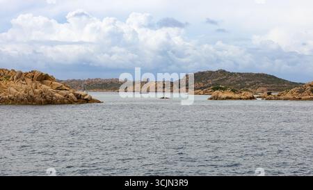 Costa rocciosa dell'isola di Santa Maria con barche a vela ancorate in acque turchesi, arcipelago la Maddalena, in Sardegna, sotto un cielo nuvoloso. Foto Stock