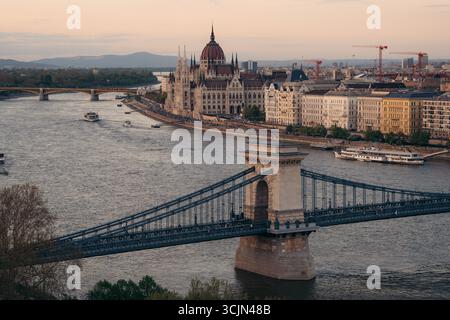 Vista del Ponte delle catene che si estende attraverso il Danubio verso l'edificio del Parlamento ungherese sotto un cielo caldo, Budapest, Ungheria. Foto Stock