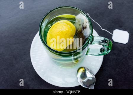 Bevanda a base di tè nero confezionata a base di erbe con birre di limone in tazza di vetro sul tavolo Foto Stock