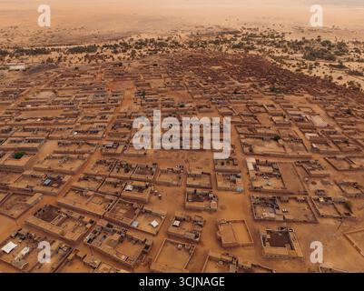 La vista aerea dei toni della terra al sole dipinge le antiche abitazioni annidate tra la vasta distesa del paesaggio desertico, Ouadane, Adrar, Mauritania. Foto Stock
