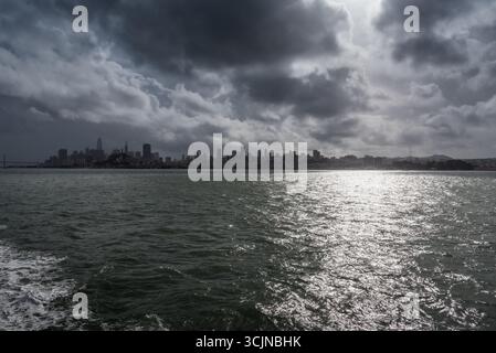 Vista della luce del sole che si riflette dall'acqua verso lo skyline della città sotto un cielo spettacolare, creando un incredibile contrasto di luce e ombra, San Francisco, California, Stati Uniti. Foto Stock