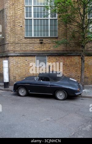 Una classica Porsche 356 convertibile è parcheggiata in una strada di Londra, con iconiche case in mattoni rossi sullo sfondo. Un simbolo di eleganza, stile vintage Foto Stock