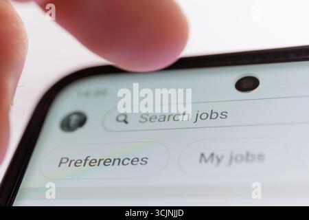 Primo piano dello schermo dello smartphone con il testo dei processi di ricerca e lo schermo a sfioramento con le dita. Concetto di mercato del lavoro, disoccupazione Foto Stock