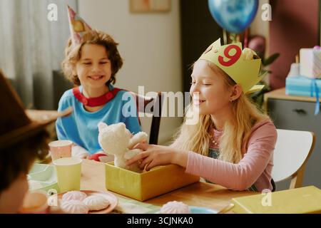 Ragazza caucasica che celebra il regalo di apertura del nono compleanno con amici sorridenti Foto Stock