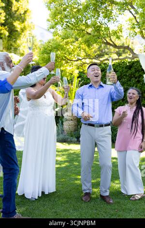 Alzando bicchieri da champagne, un gruppo eterogeneo che celebra festosi brindisi di nozze all'aperto Foto Stock
