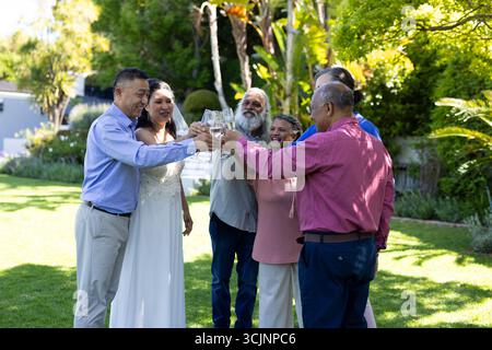 Gli amici anziani brindano con bicchieri da vino nel giardino soleggiato, festeggiando insieme Foto Stock