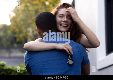 Una giovane coppia che abbraccia l'aria aperta, una donna sorride gioiosamente mentre tiene le chiavi in mano Foto Stock