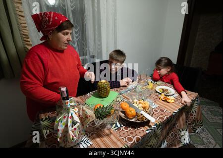 Una donna e due bambini siedono a un tavolo carico di frutta. Sembra che la donna stia preparando un'insalata di frutta. La scena è intima e familiare. Foto Stock