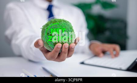 Un uomo d'affari che detiene un globo coperto di muschio con un brillante testo NET ZERO, che simboleggia la responsabilità aziendale, la sostenibilità, la neutralità del carbonio e cl Foto Stock