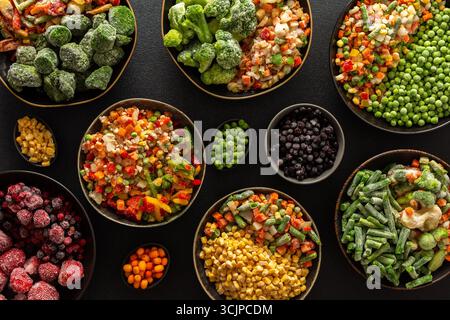 Una varietà di verdure e frutta congelate disposte in piatti, su sfondo scuro, catturando l'essenza della conservazione estiva per i pasti invernali Foto Stock