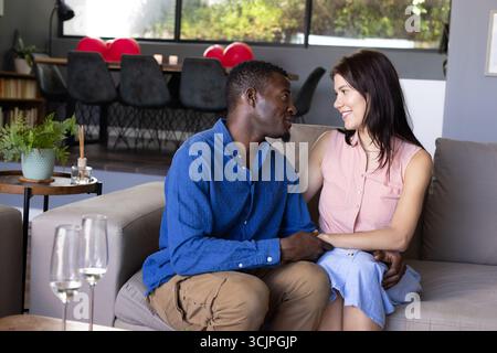 La coppia si siede sul divano a casa, condividendo momenti amorevoli e sorridendo calorosamente Foto Stock