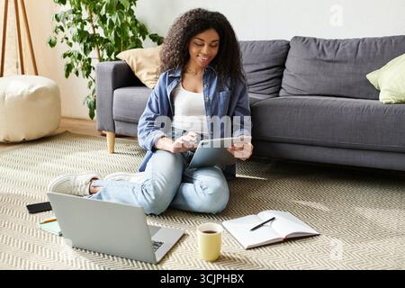 Una giovane donna dai capelli ricci si impegna a lavorare come freelance mentre è circondata da un ambiente accogliente. Foto Stock