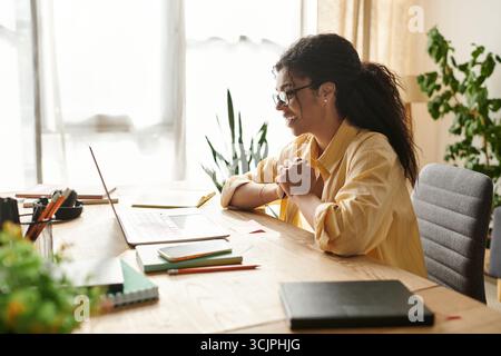 Una giovane donna dedicata con capelli ricci lavora da remoto a casa, trasudando produttività. Foto Stock