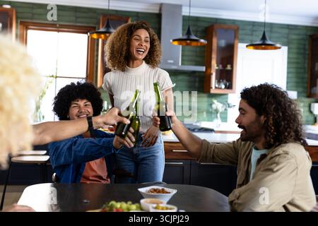 I giovani amici brindano con bottiglie di birra in un'accogliente cucina, godendosi dei bei momenti Foto Stock