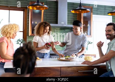 I giovani amici preparano spuntini e si divertono a conversare in una cucina moderna Foto Stock