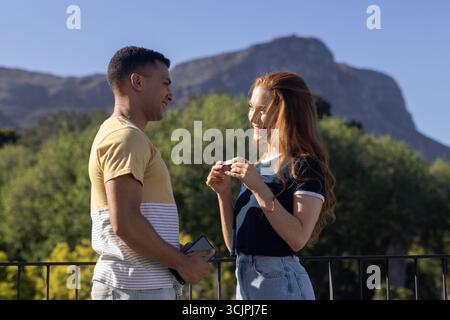 Giovane coppia che si diverte a conversare all'aperto, sorridendo e tenendo lo smartphone insieme Foto Stock