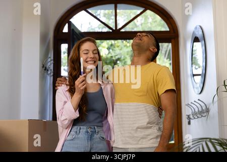 Giovane coppia che celebra il risultato positivo del test di gravidanza a casa, abbracciando con gioia Foto Stock