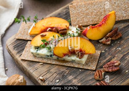 Croccante ricoperto di formaggio blu, fette di pesca e miele su sfondo chiaro Foto Stock