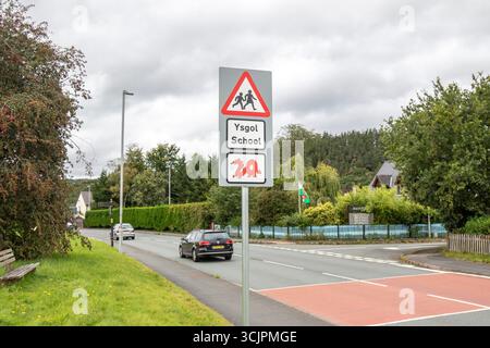 Segnale di avvertimento triangolare rosso per i conducenti per la pattuglia di attraversamento della scuola sul posto fuori dalla scuola gallese (ysgol) con insolito simbolo di drago rosso sotto. Foto Stock
