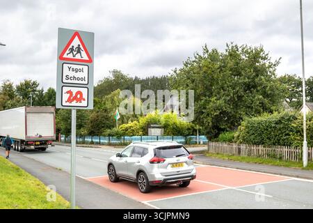 Segnale di avvertimento triangolare rosso per i conducenti per la pattuglia di attraversamento della scuola sul posto fuori dalla scuola gallese (ysgol) con insolito simbolo di drago rosso sotto. Foto Stock