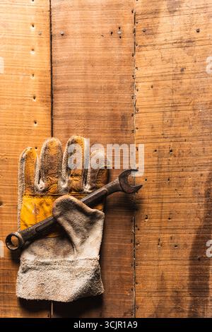 Guanti da lavoro in pelle con una chiave arrugginita e dollari americani su un tavolo da lavoro rustico in legno Foto Stock