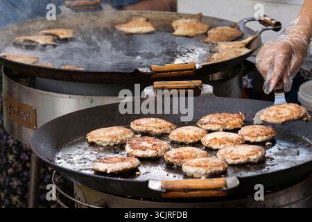 Un grande grill rotondo serve arrostire le polpette di pesce. Cotoletta di pesce fresco in una padella grill. Festa del barbecue nel parco cittadino. Fast food di strada. Foto Stock
