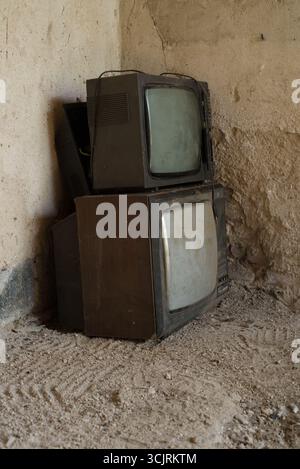 Bulanka, Repubblica Ceca, 28 agosto 2025 - due vecchi televisori d'epoca impilati in una stanza rustica polverosa con pareti e terreno testurizzati, simbolo di retro te Foto Stock
