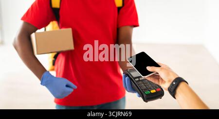 Uomo nero che tiene il cliente della macchina del POS che paga con lo smartphone Foto Stock