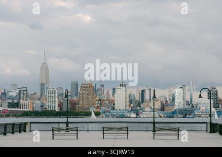 Le panchine si affacciano sul lungomare con una vista dello skyline della città sotto il cielo nuvoloso alla luce del pomeriggio. Foto Stock