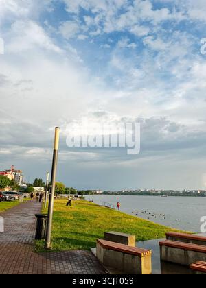 Tarnopil, Ucraina - 10 agosto 2025: Tranquilla passerella lakerside con erba verde, panchine e vista sulla città. Foto Stock
