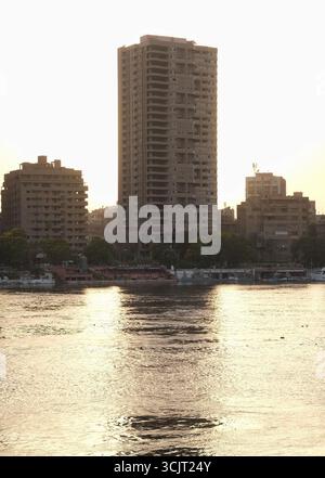 Alti edifici lungo il fiume Nilo al tramonto al Cairo, in Egitto, che mostrano riflessi dorati sull'acqua e sull'architettura urbana al tramonto Foto Stock
