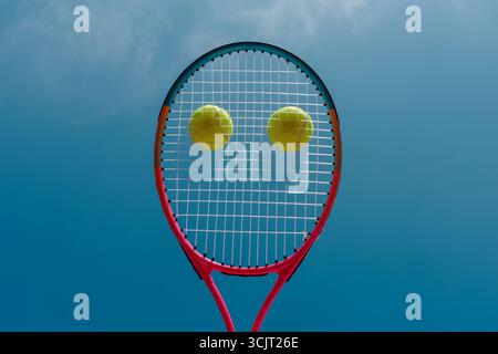 Primo piano concettuale della racchetta da tennis con due palline che rendono il viso contro il cielo blu un design sportivo minimalista creativo con spazio per copiare Foto Stock