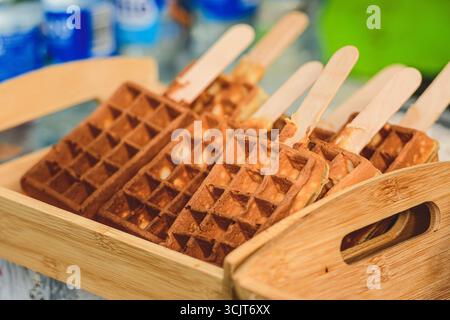 Waffle dorati croccanti serviti su bastoncini di legno, disposti ordinatamente in un vassoio di bambù Un tocco creativo e portatile per un dolce classico Foto Stock