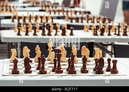 File di scacchiere con pezzi in bianco e nero disposti in modo ordinato, disposti sui tavoli, probabilmente per un torneo di scacchi pubblico o un evento all'aperto Foto Stock
