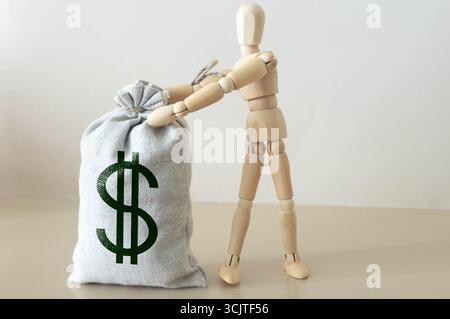 Uomo che tira su una corda un sacco di soldi, un muro grigio sullo sfondo Foto Stock