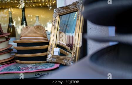 Una pila di cappelli estivi e uno specchio decorato nella vetrina di un tradizionale negozio di cappelli nel quartiere Prenzlauer Berg di Berlino. Foto Stock