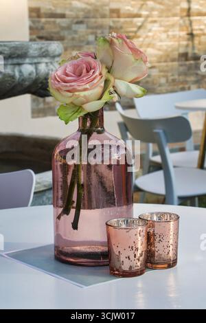 tavoli decorati, grande bottiglia di vaso trasparente con due bicchieri, colori pastello rosa, tavolo e sedie, mobili da giardino all'aperto Foto Stock