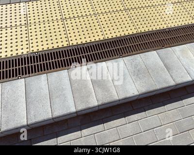 marciapiede urbano con gradini in cemento e indicatori tattili gialli per i non vedenti. Foto Stock