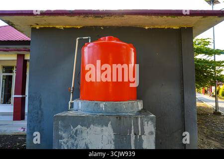 Il serbatoio dell'acqua arancione per esterni si trova su un supporto in calcestruzzo fissato alla parete di un edificio ed è adatto per progetti di costruzione o infrastrutture. Foto Stock
