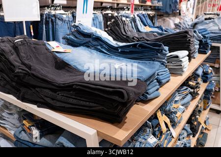 Pile di jeans blu disposte ordinatamente su scaffali di legno in un negozio di abbigliamento, che espone la moda al dettaglio e il concetto di merchandising Foto Stock