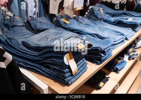 Pile di jeans blu disposte ordinatamente su scaffali di legno in un negozio di abbigliamento, che espone la moda al dettaglio e il concetto di merchandising Foto Stock