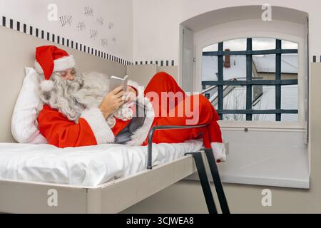 Babbo Natale riposa con un piccolo libro su un letto a castello in prigione Foto Stock