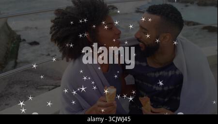 Coppia seduto avvolto in una coperta grigia chiara su una sporgenza di cemento tramite ringhiera, tenendo in mano i coni del gelato Foto Stock